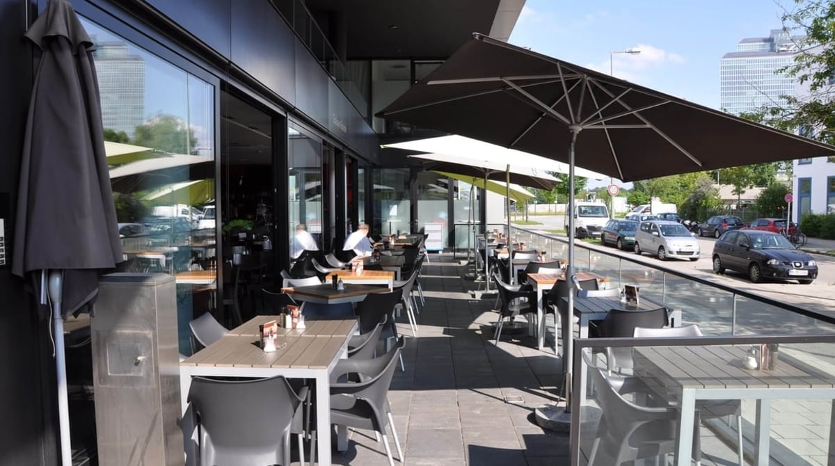 Terrasse des Goloseo Grande mit Tischen, Stühlen und Sonnenschirmen vor der Fensterfront des Restaurants