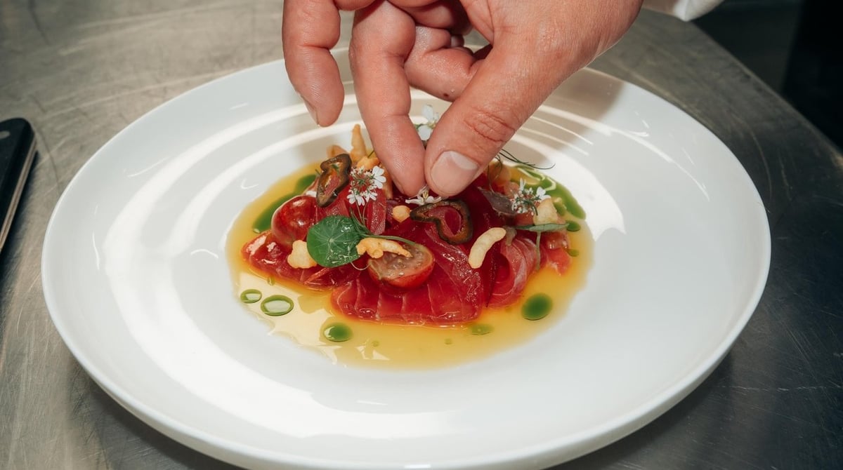Hände beim Anrichten eines Tatars mit Tomaten und Kräutern in der Küche