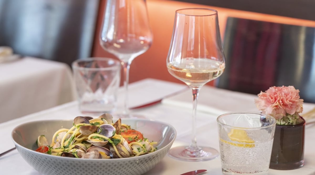 Spaghetti mit Venusmuscheln und Tomaten in einer grauen Schale, daneben Weißwein und Rotwein