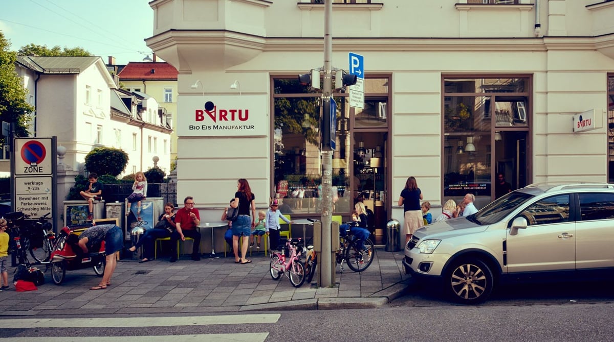 Ladenfront der Bartu Bio Eismanufaktur an der Straßenecke in Schwabing, davor sitzen und stehen Gäste