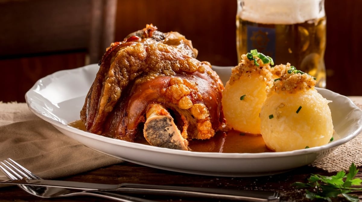 Schweinshaxe mit zwei Knödeln und Soße auf einem tiefen Teller