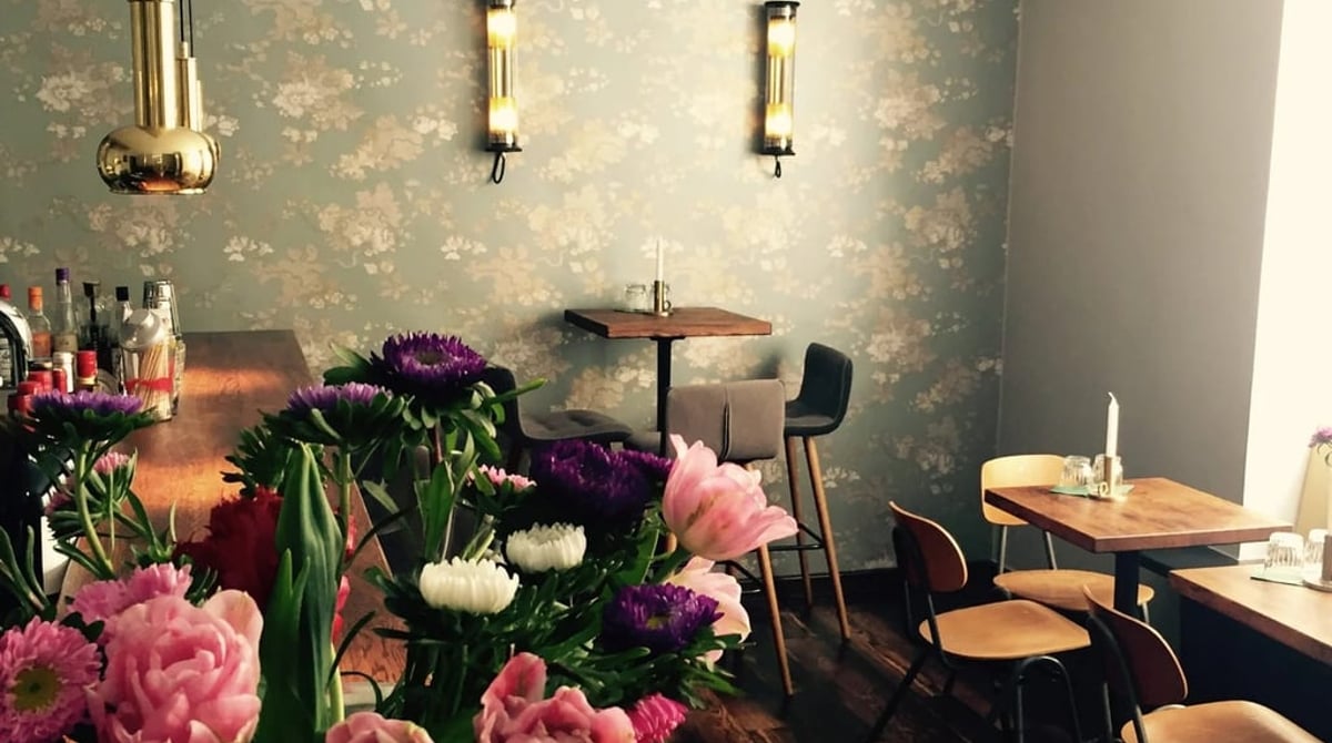 Gastraum der Bodeguita mit Blumensträußen, geblümter Tapete und Holztischen