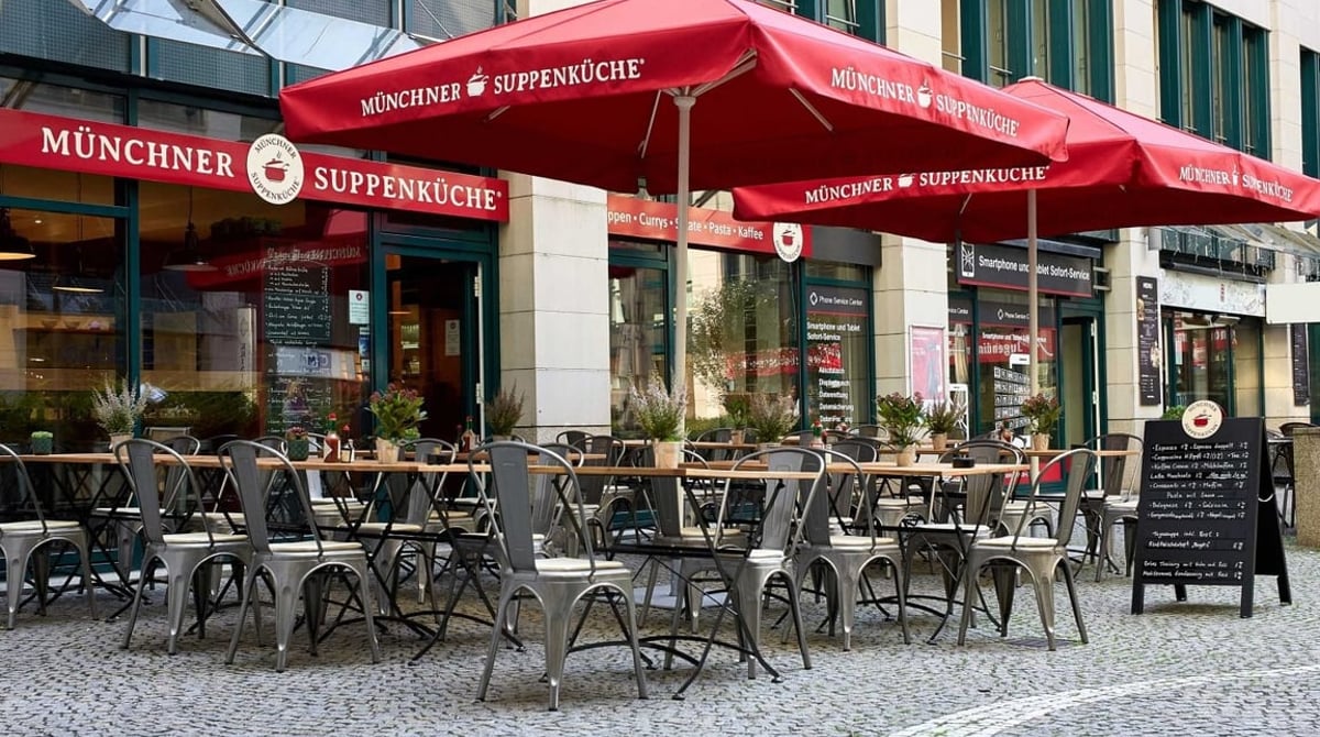 Außenbereich der Münchner Suppenküche in der Sendlinger Straße mit roten Schirmen und Tischen