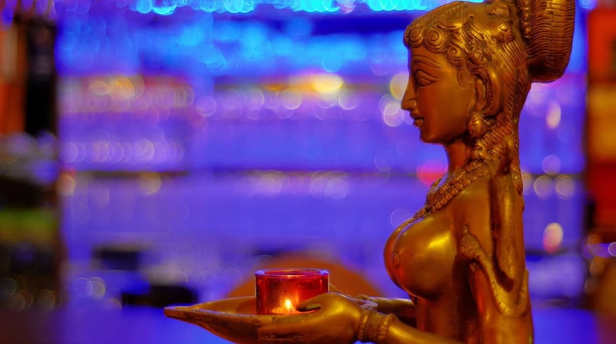 Goldene Bronzefigur mit einer Kerzenschale vor bunt leuchtendem Hintergrund