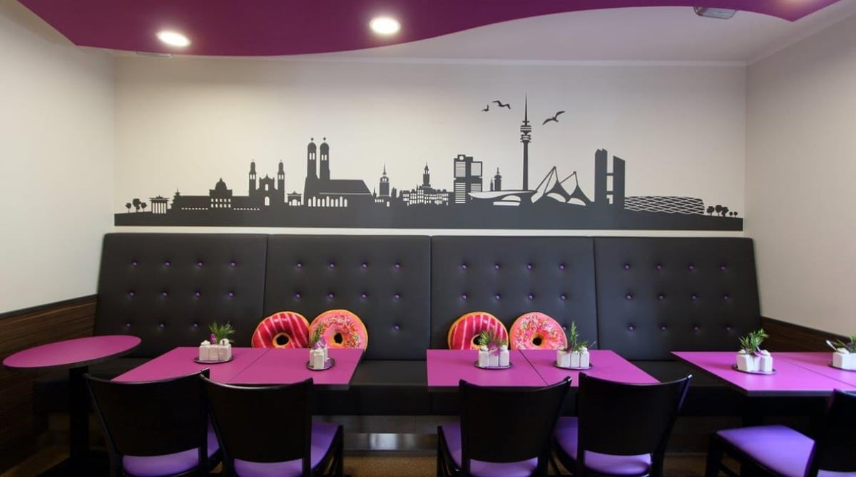 Gastraum des Stemerowitz mit gepolsterter Sitzbank, pinken Tischen und einer Münchner Skyline an der Wand