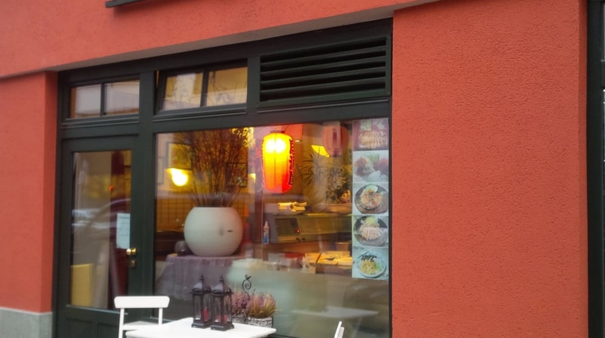 Rot verputzte Fassade des Bento Ya an der Augustenstraße in München mit beleuchteter Papierlaterne im Fenster und Tisch vor der Tür