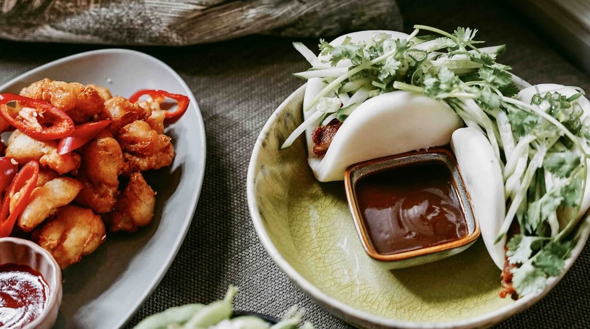 Bao-Bun mit Dip und Kräutersalat, daneben frittierte Stücke mit roten Chilistreifen
