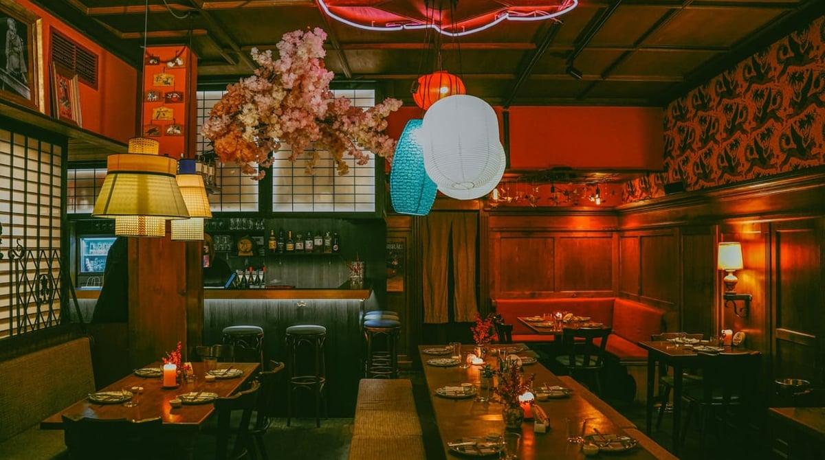 Gastraum des Ciao Chang mit dunklem Holz, roter Neonschrift, Lampions und Kirschblüten über den Tischen
