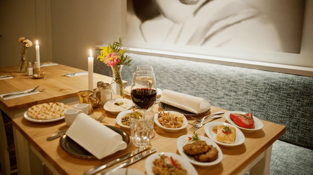 Gedeckter Tisch mit mehreren Vorspeisen und Kerze vor einer Sitzbank in der Taverna Melina