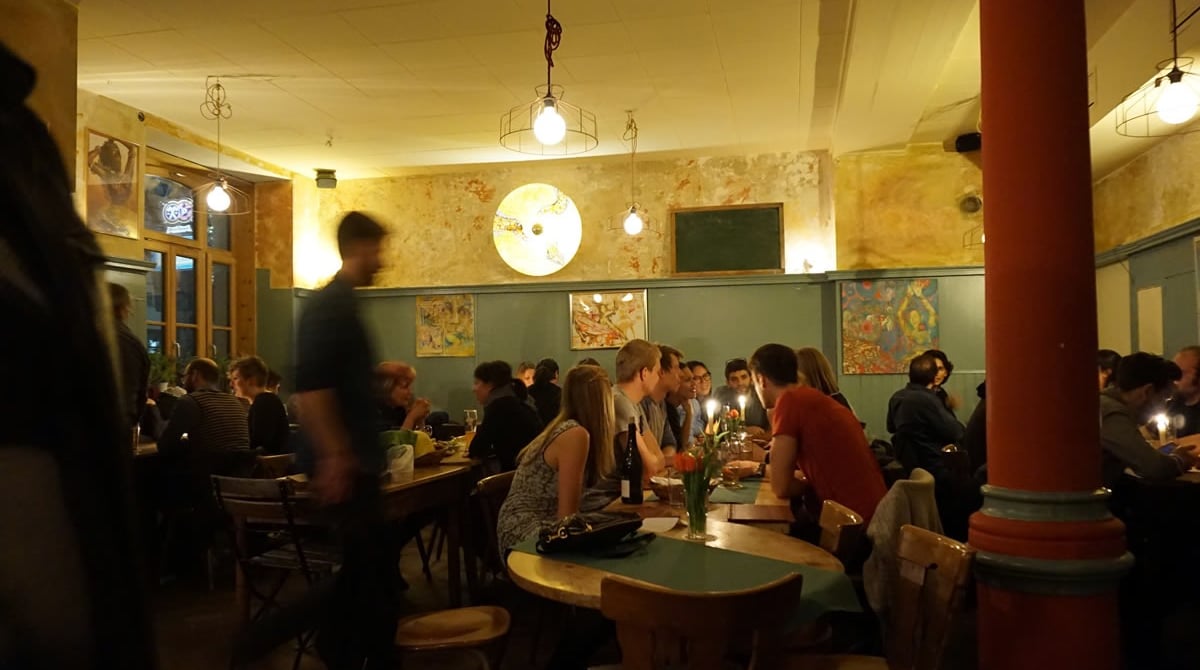 Gastraum der Yol Taverne mit rotem Pfeiler, Holztischen und Wandbildern