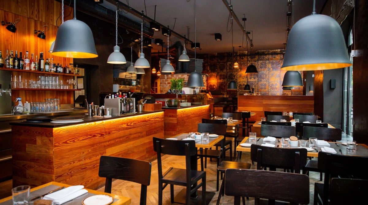 Gastraum mit Holzbar, schwarzen Pendelleuchten und gedeckten Tischen in einem MOZZAMO-Restaurant