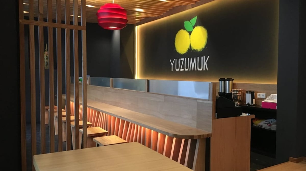 Gastraum des Yuzumuk mit Holzdecke, Eichenholz-Counter, Hockern und beleuchtetem Logo an der Wand