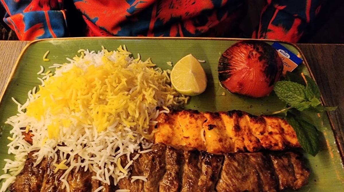 Kebab mit Safranreis, gegrillter Tomate und Limette auf einem grünen Teller