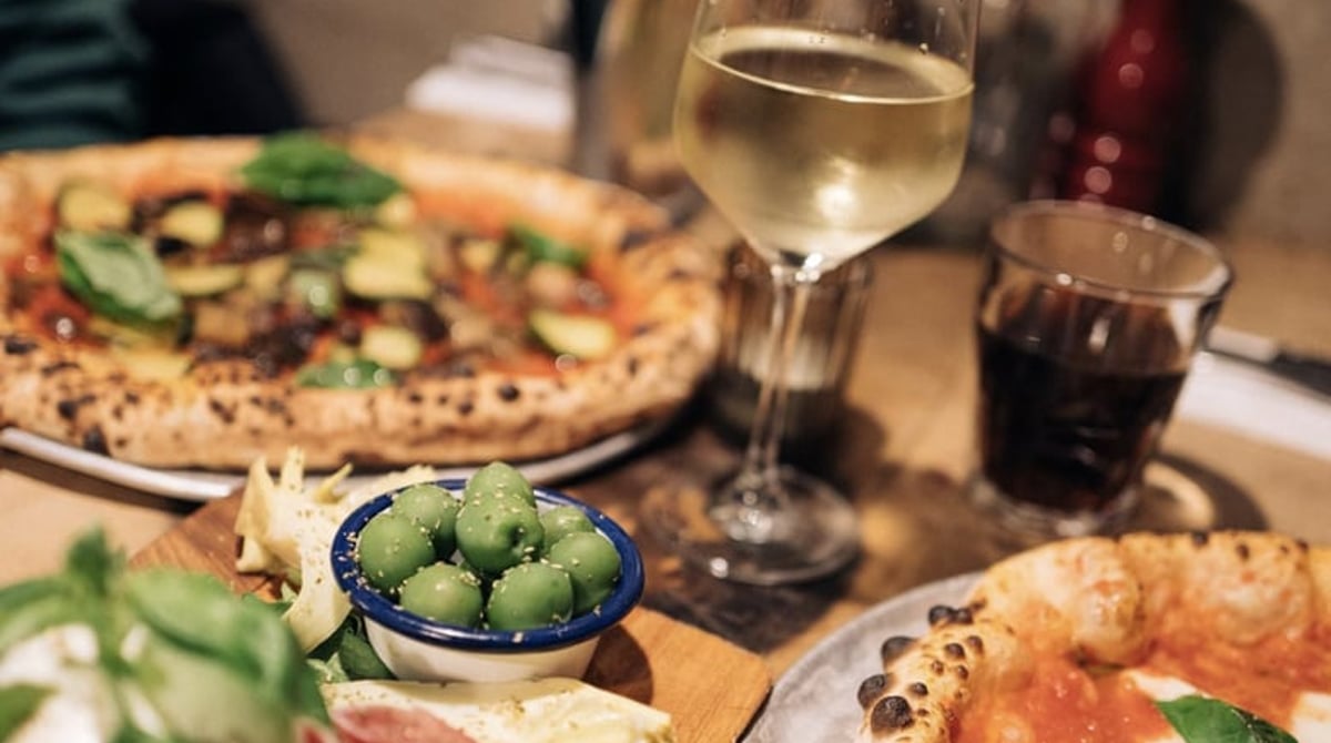 Gedeckter Tisch mit Pizza, Antipasti, Oliven und Weißwein