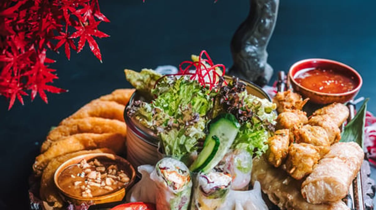 Vorspeisenplatte mit Sommerrollen, Frühlingsrollen, Teigtaschen, Salat und Dips auf einer Holzscheibe