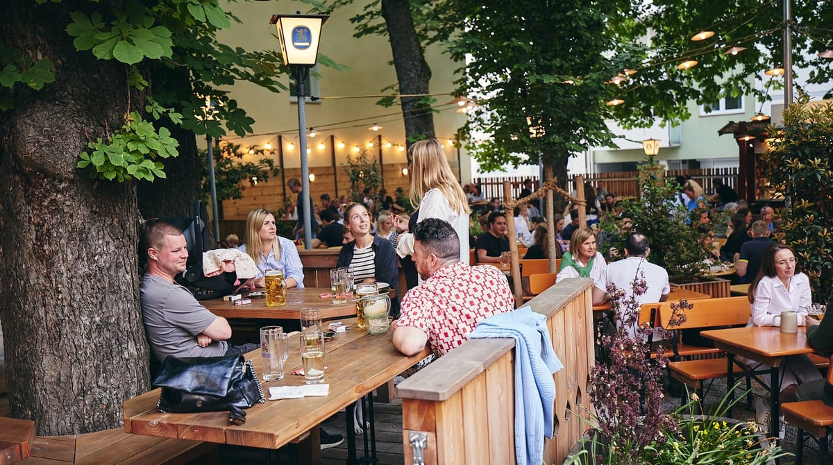Gäste an Holztischen im Biergarten der Max Emanuel Brauerei unter alten Kastanien