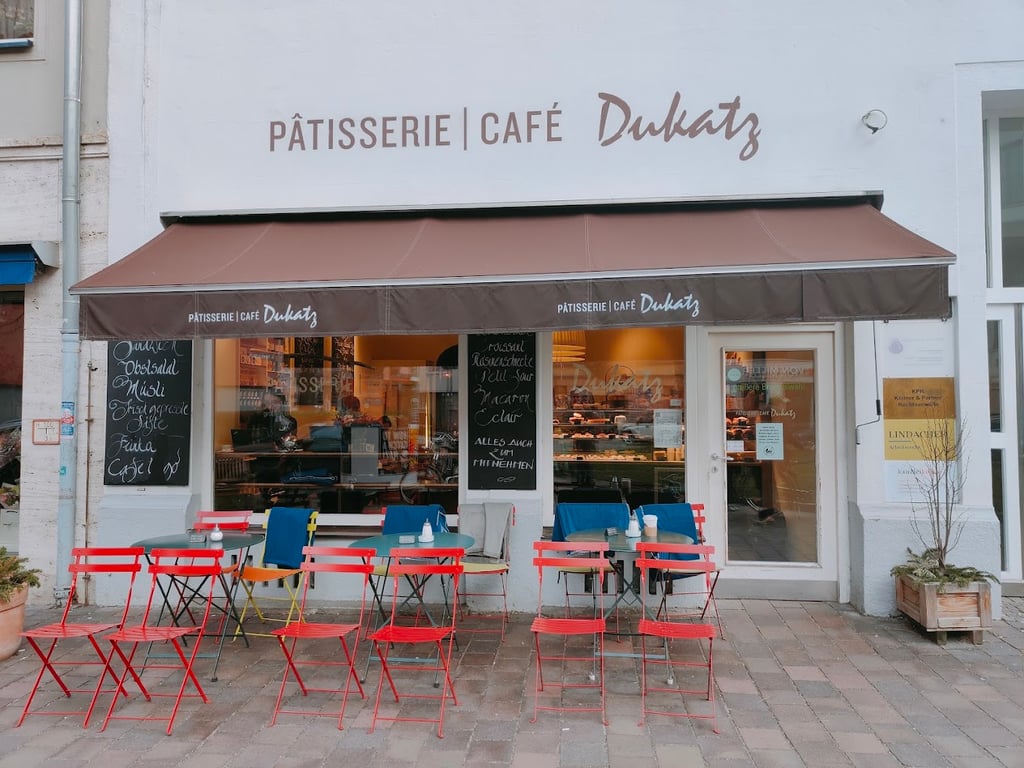 Pâtisserie Café Dukatz mit Markise und roten Stühlen vor dem Laden