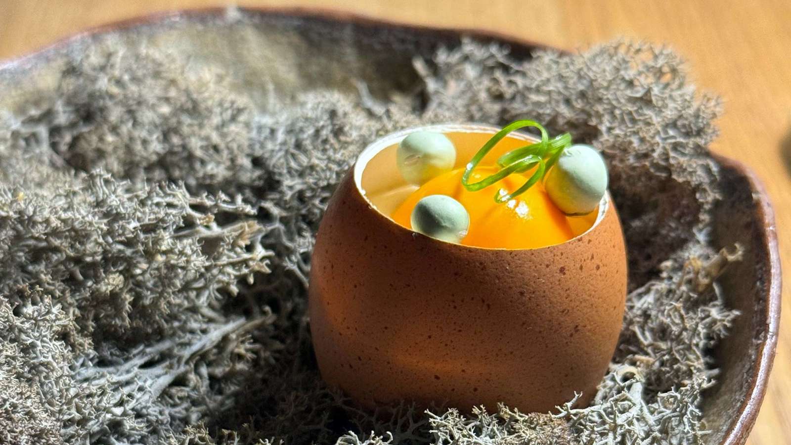 Braune Eierschale auf grauem Moos, gefüllt mit orangegelber Emulsion und grünen Kugeln