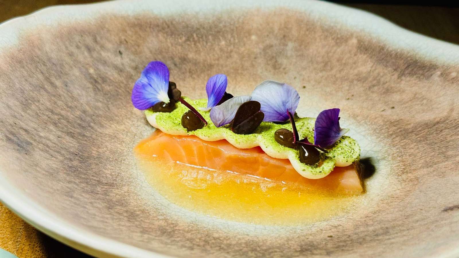 Saiblingstranche mit Apfel-Meerrettich-Baiser, essbaren Blüten und Kräuterstaub auf einem Teller