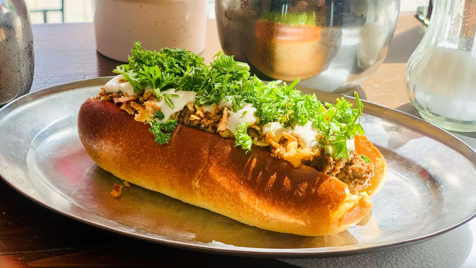 Getoastetes Brioche-Brötchen „Witch“ mit Hackfleisch, Sesamcreme, Röstzwiebeln und Petersilie auf einem Metallteller