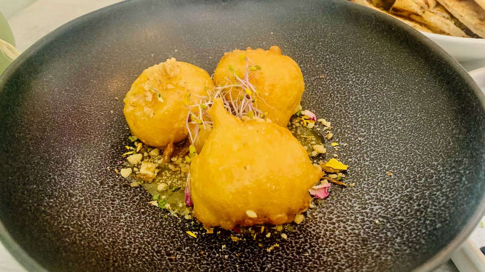 Drei frittierte Kroketten mit Walnüssen und Blütenblättern auf einem dunklen Teller