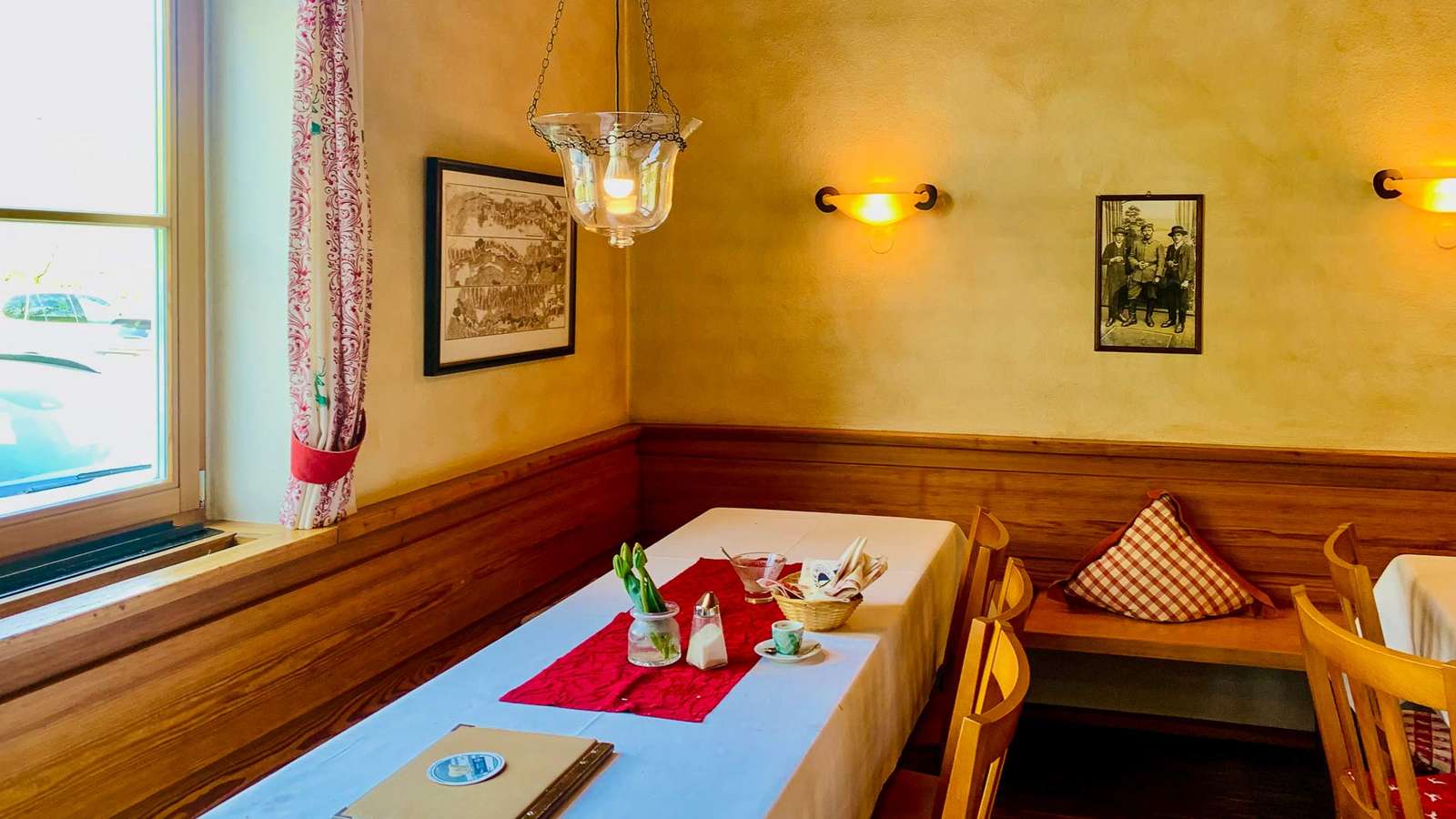 Holzgetäfelte Gaststube mit gedecktem Tisch, rotem Tischläufer, Eckbank und Hängelampe