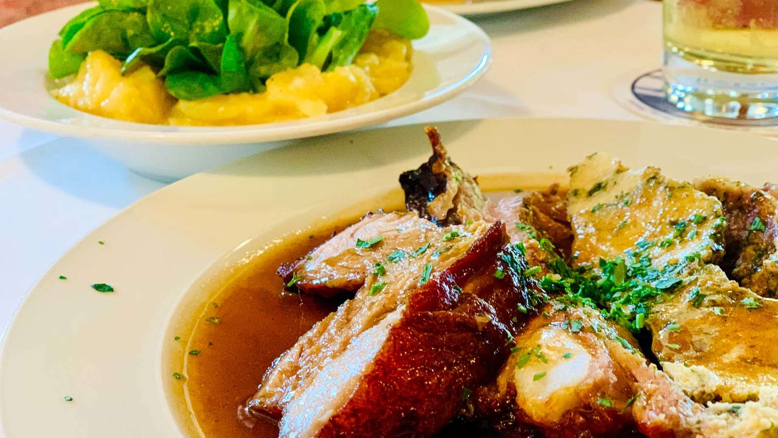 Schweinebraten mit dunkler Soße und gefüllte Kalbsbrust mit Schnittlauch, dahinter Kartoffel-Feldsalat