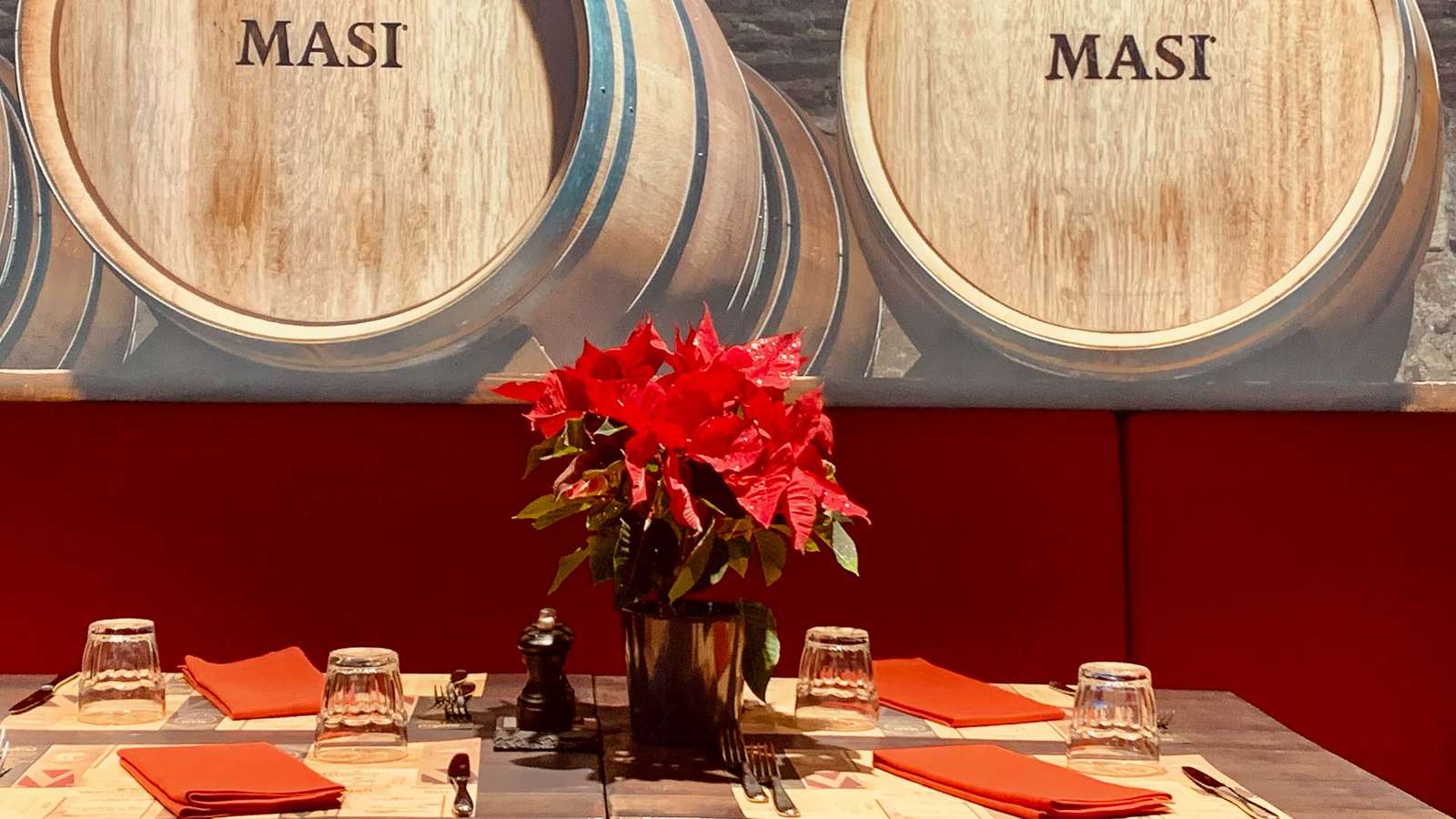 Gedeckter Tisch vor roter Polsterbank und Masi-Weinfässern mit Weihnachtsstern in der Masi Wine Bar