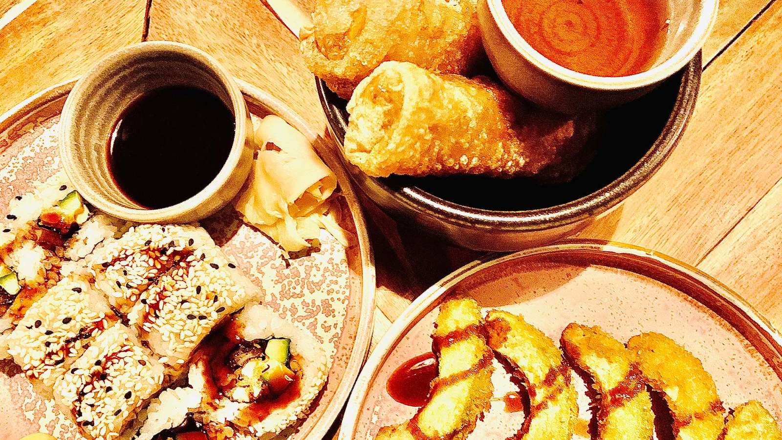 Frittierte Avocado-Schnitze, Frühlingsrollen und Inside-out-Sushi mit Dips auf einem Holztisch im Ahimsa