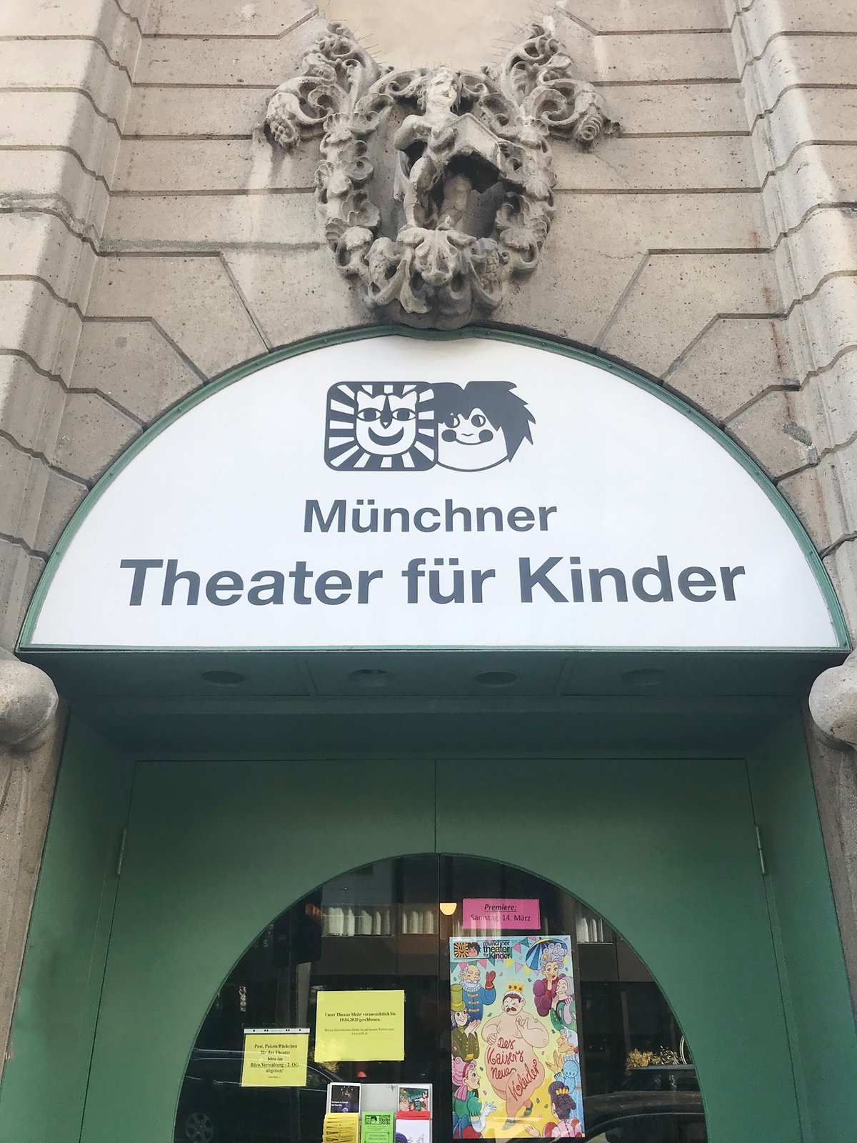 Facade of Münchner Theater für Kinder entrance with a carved stone crest above the sign, indicating a children's theater in Munich, Germany.