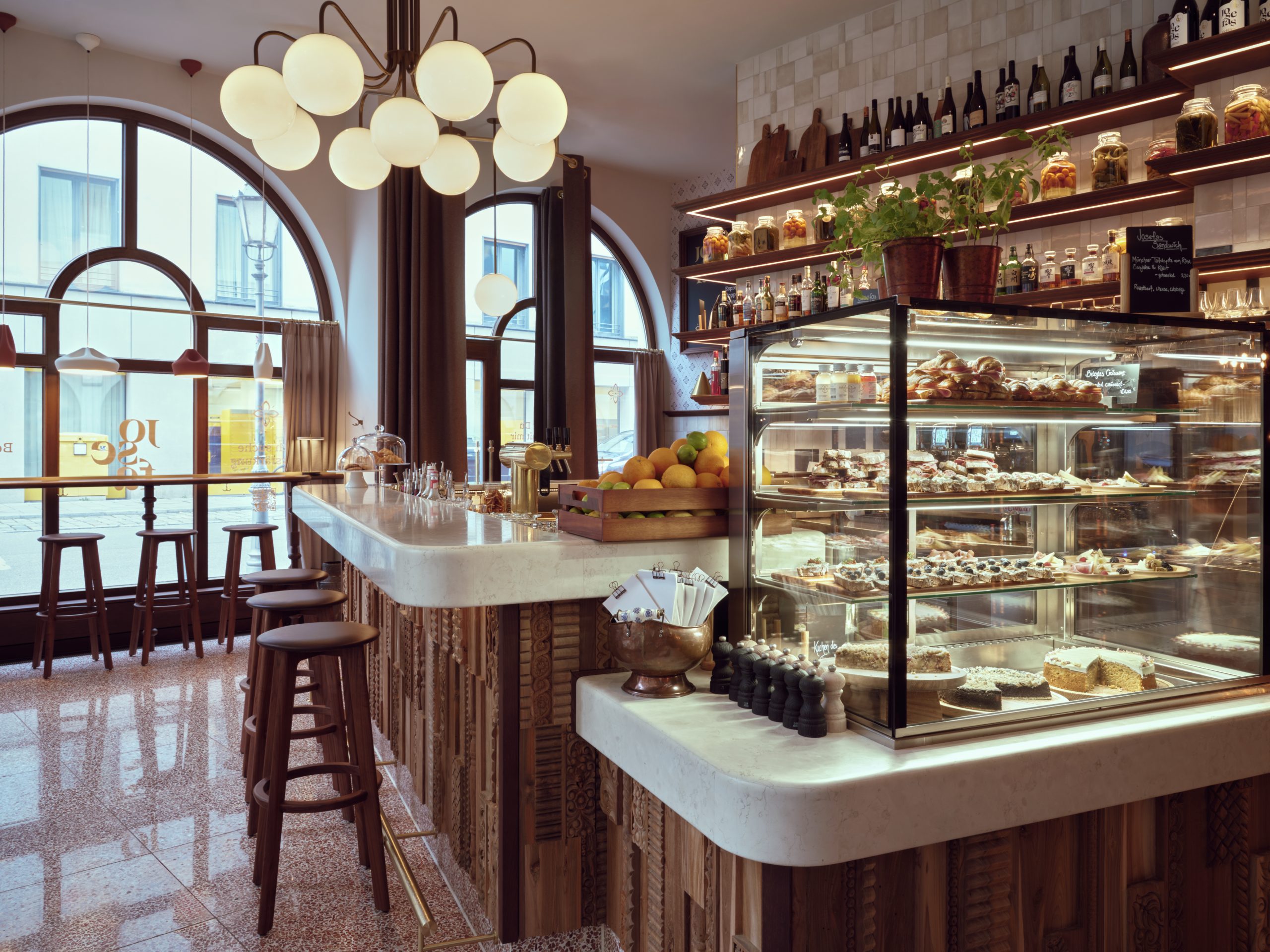 Cafe interior with curved windows, globe chandelier, and a pastry display case along a marble bar.