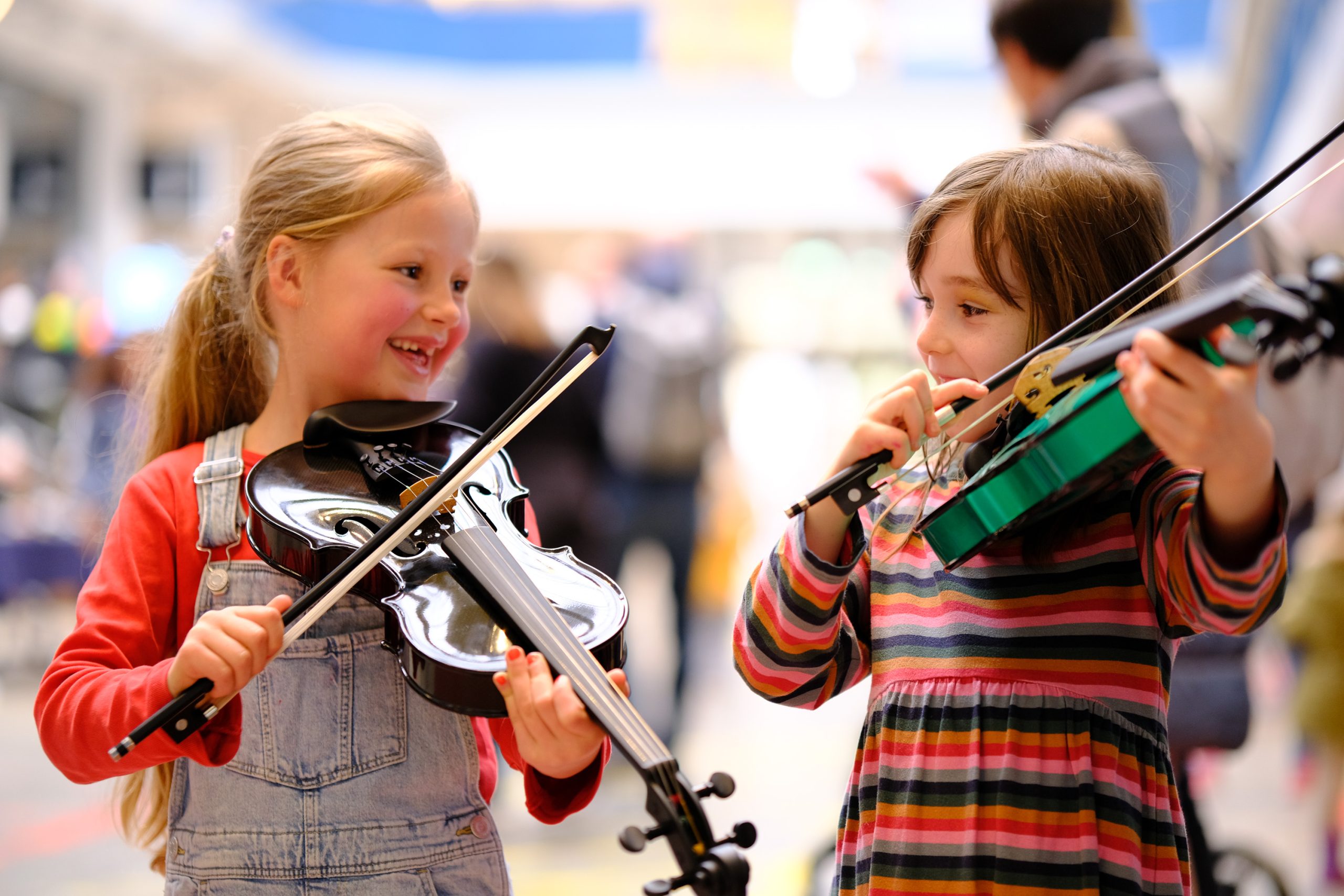 Zwei kleine Mädchen probieren lachend zwei Geigen aus beim Musikfestival "Der Gasteig brummt"