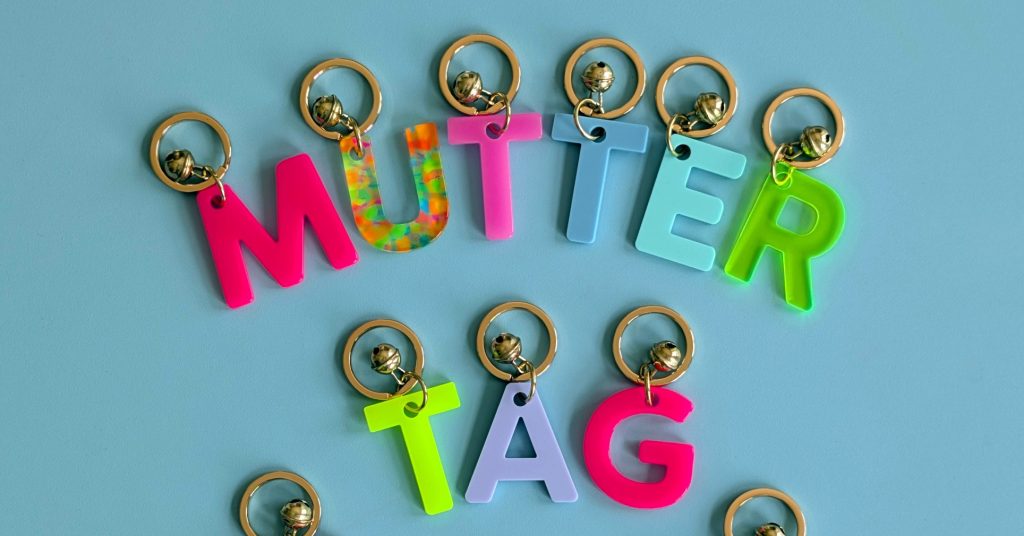 Colorful plastic letter keychains spelling 'WUTTER TAG' arranged on a blue background with small metal bells attached to each letter.