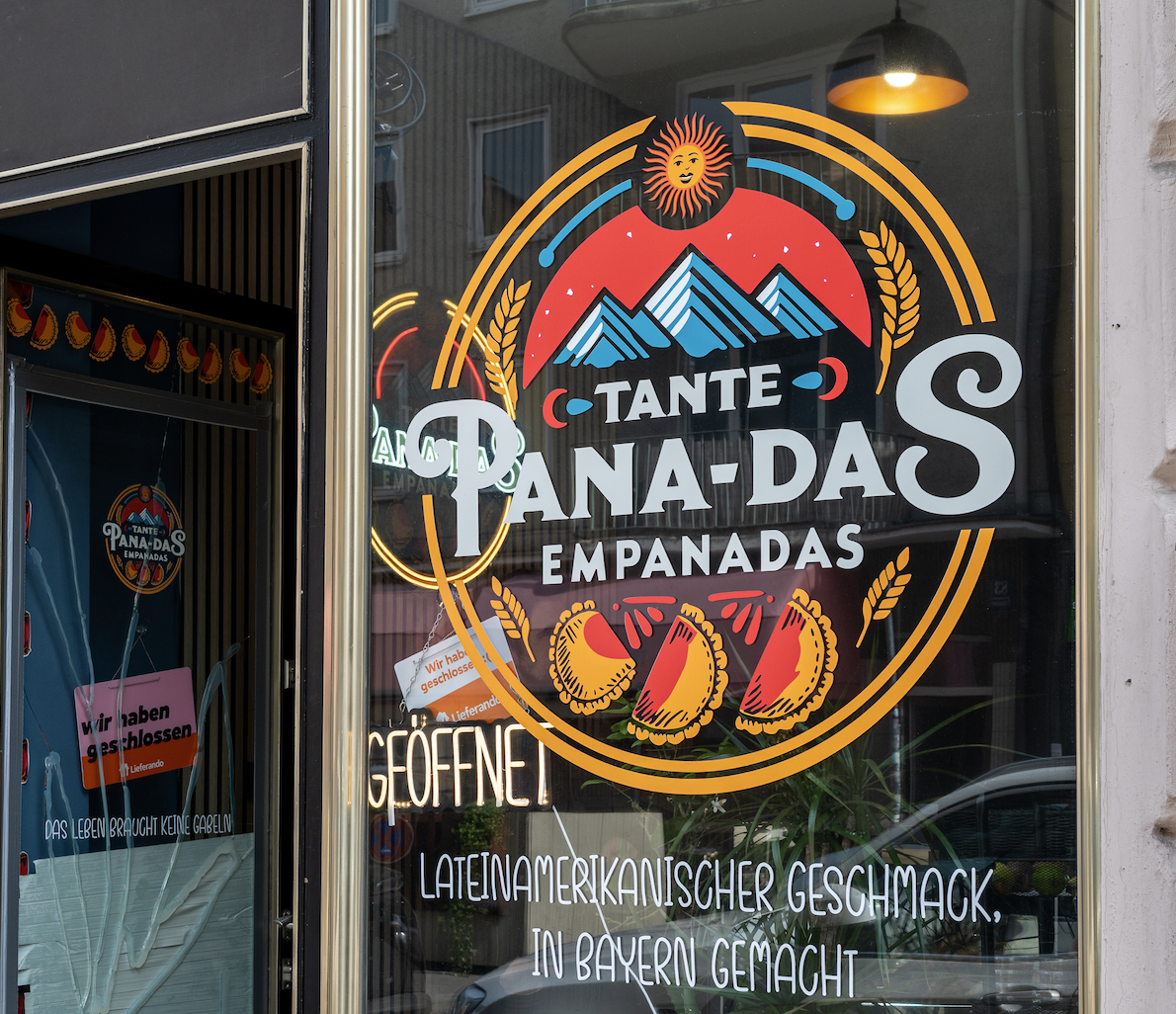 Colorful storefront window sign for Tante Panadas Empanadas with mountains and sun graphic and orange circular border to convey the brand message.