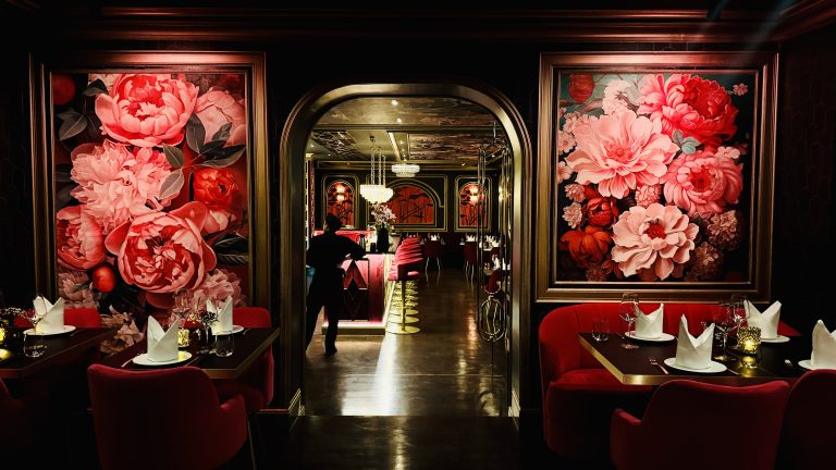 Elegant restaurant dining room with large pink floral wall panels, archway entrance, and red upholstered chairs. Conveys a luxurious, romantic dining ambiance.