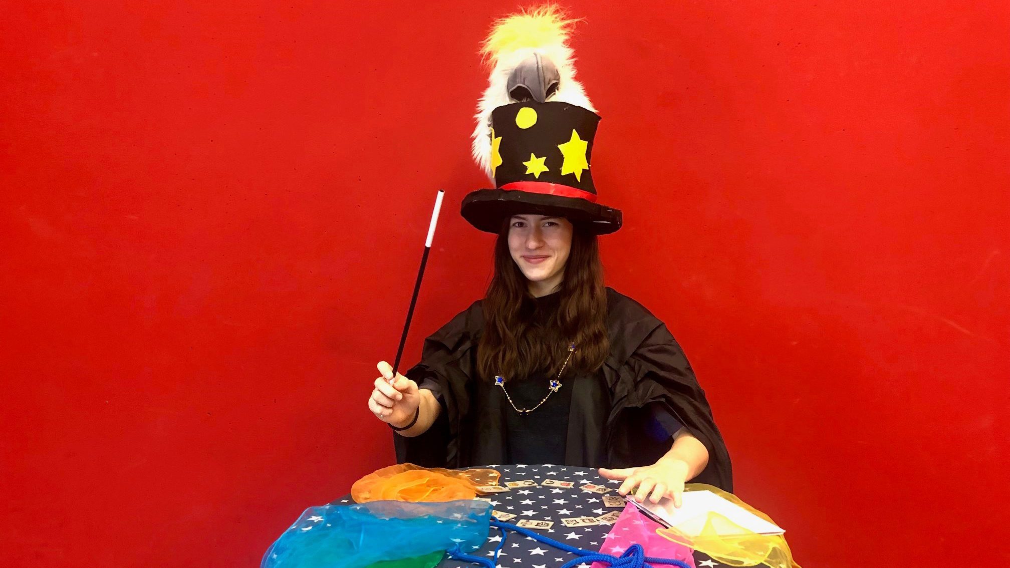 Woman in a magician costume with a tall starry hat and wand, against a red backdrop.