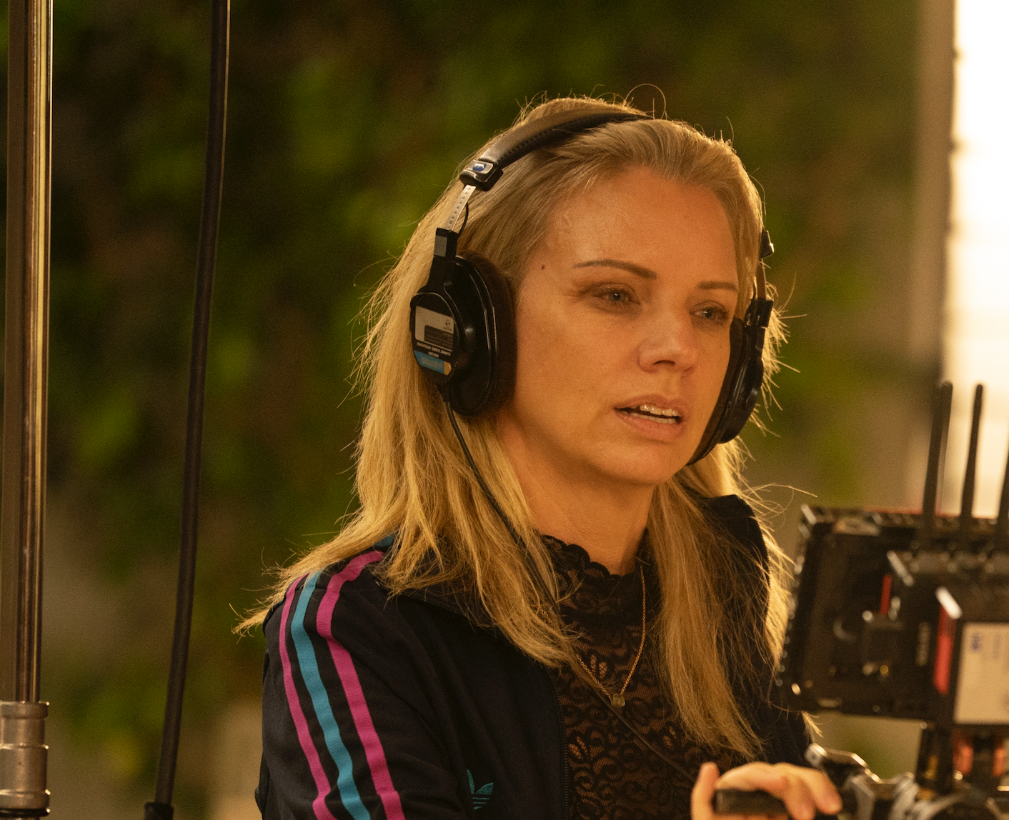 Woman with large over-ear headphones operating a camera rig in an outdoor setting, focused on her work in the night light.