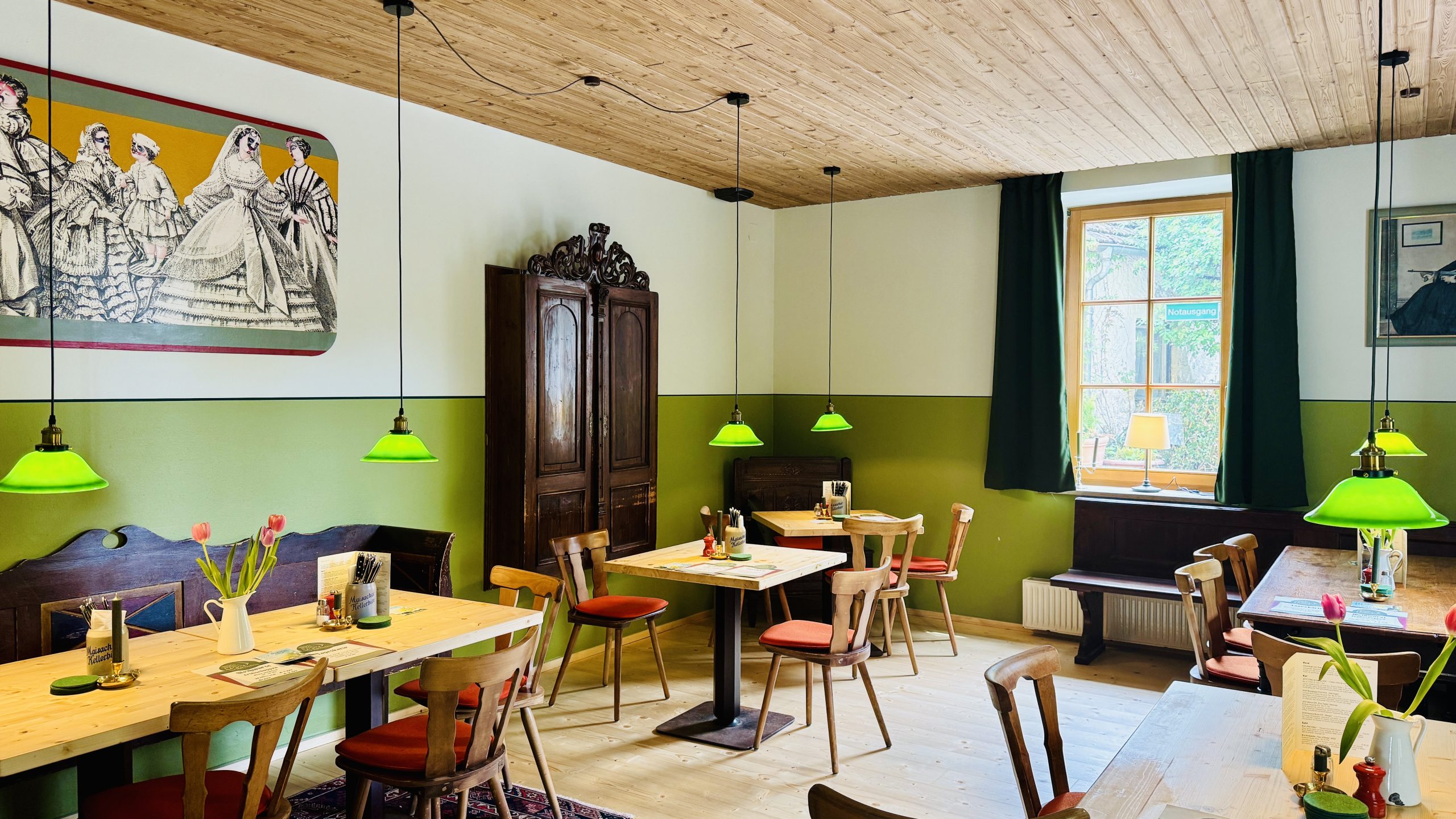Cozy cafe interior with wooden ceiling, olive-green walls, and lime green pendant lights over wooden tables and chairs using natural daylight from a window.