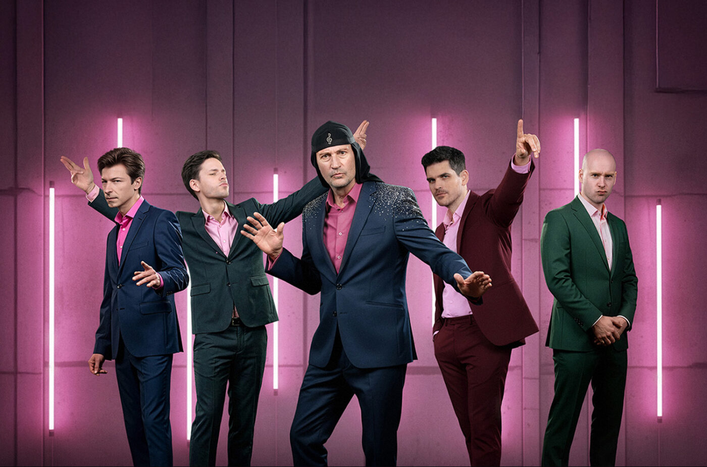 Five men in colorful suits pose dramatically in a pink neon-lit studio.