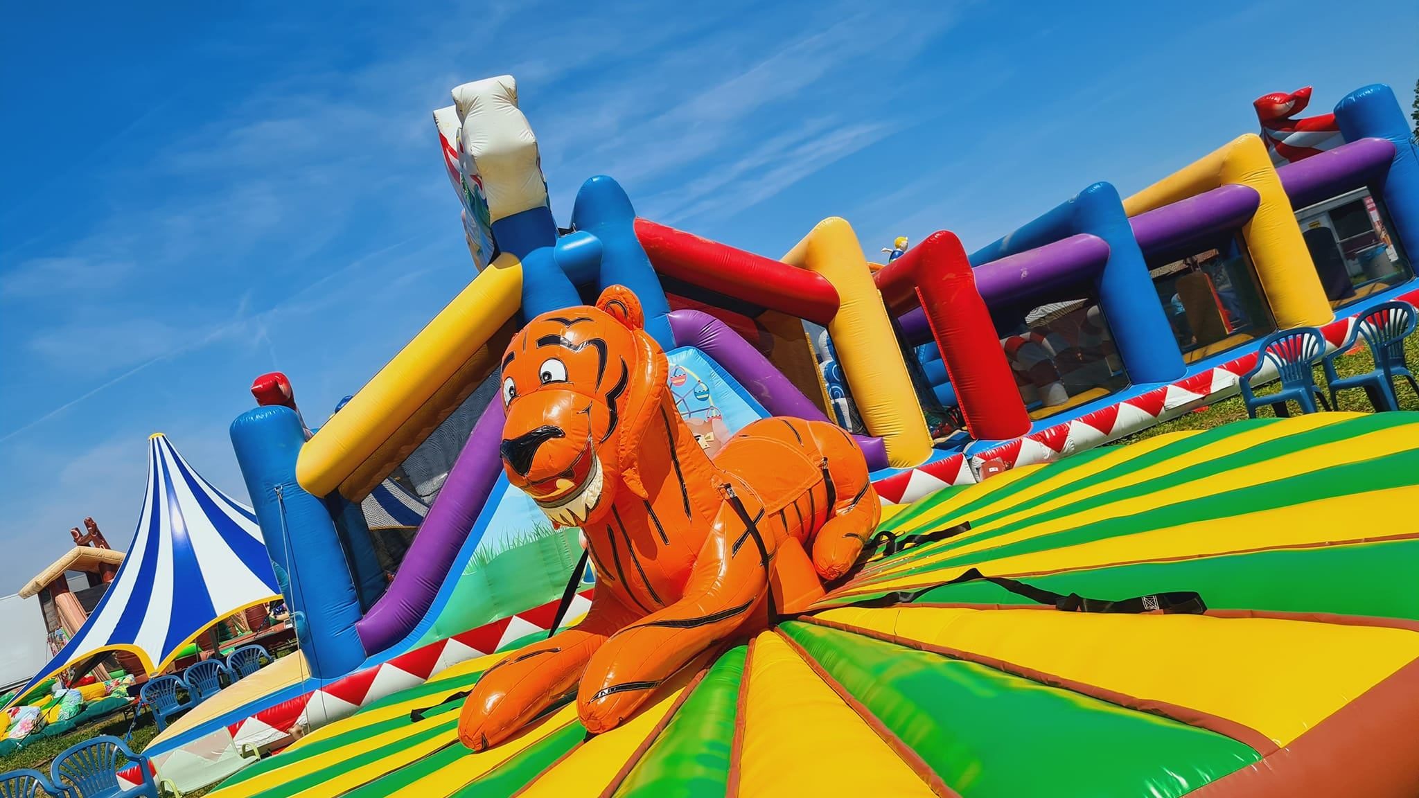 Bright inflatable slide structure in primary colors with a tiger balloon at a sunny outdoor fair.