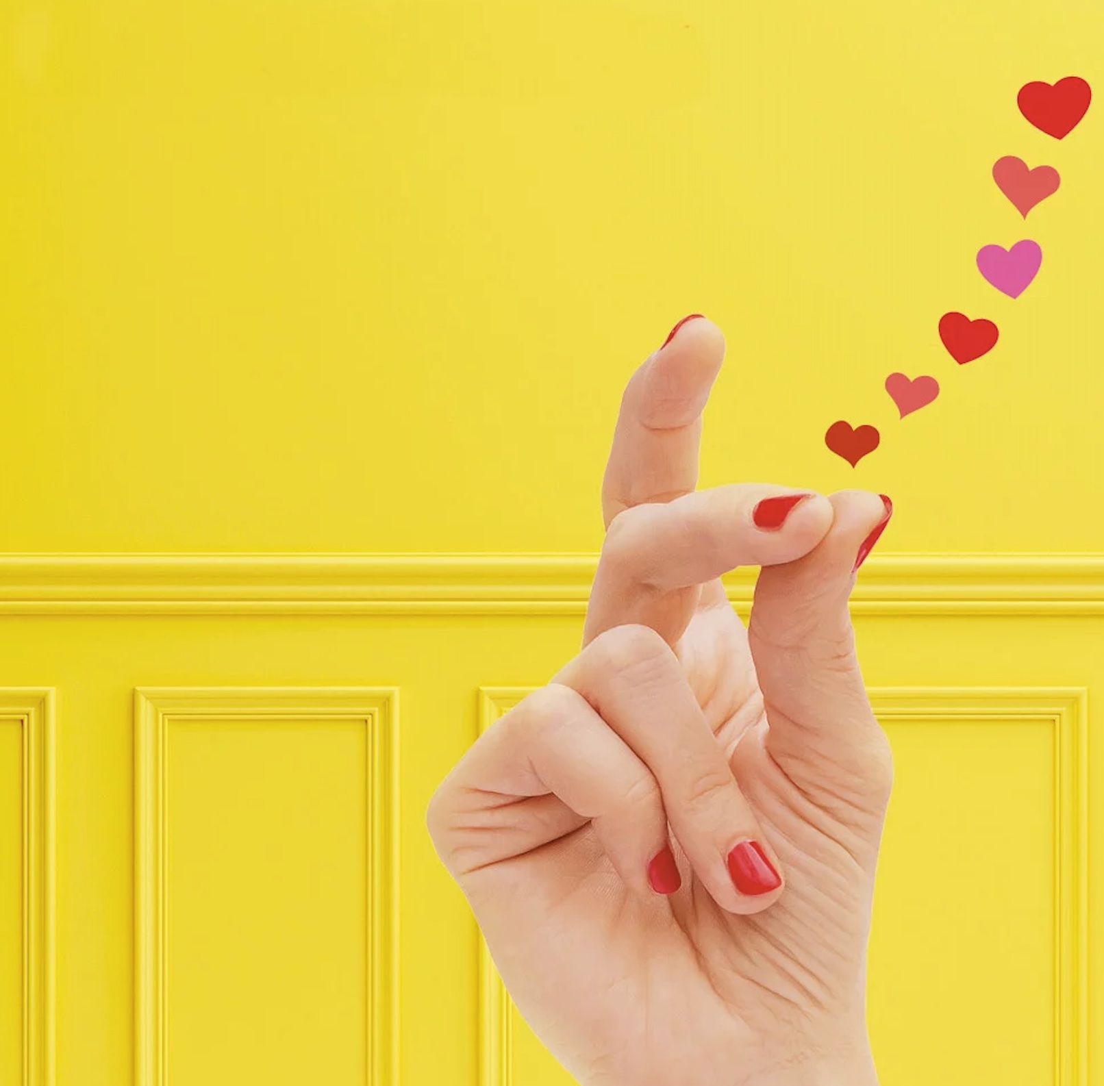 Close-up of hands making a finger heart against a bright yellow door, with small red and pink hearts to the right