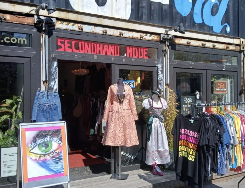 Vintage-Store-Tage-muenchen-Studio of Colours - IN München - Das Stadtmagazin Open secondhand clothing store with two mannequins in dresses outside and a rack of colorful shirts nearby.