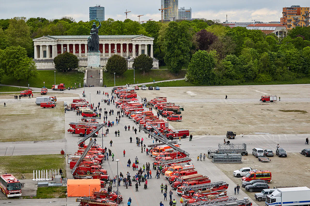 freiwillige feuerwehr - IN München - Das Stadtmagazin Row of red fire engines lined up on a wide plaza with a statue and colonnaded monument behind the scene.