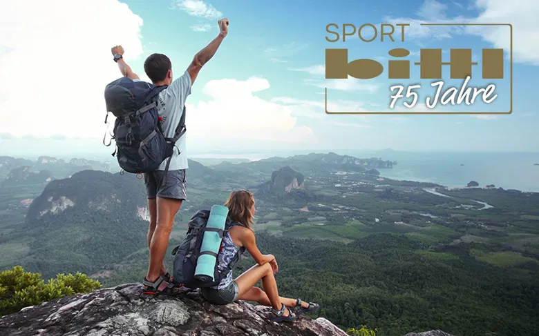 header_Sport bittl - IN München - Das Stadtmagazin Two hikers with backpacks stand on a rocky lookout, overlooking a valley and coastline; banner reads “SPORT bhh 75 Jahre.”