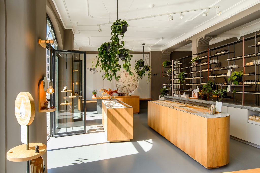 Bright boutique interior with wooden display counters, tall metal shelving, and hanging plants.