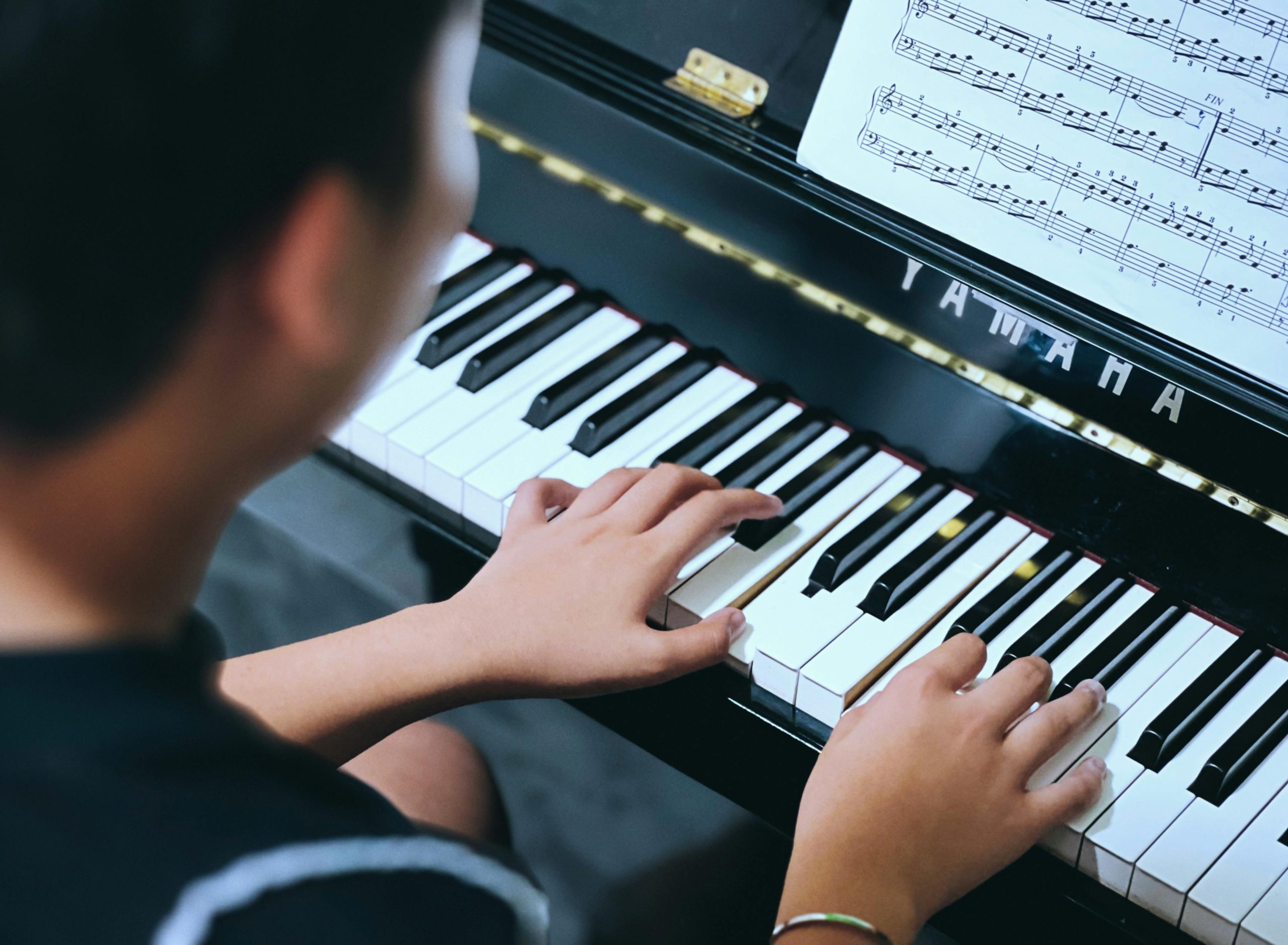 Child or young person playing piano, hands on keys with sheet music in view on a grand piano