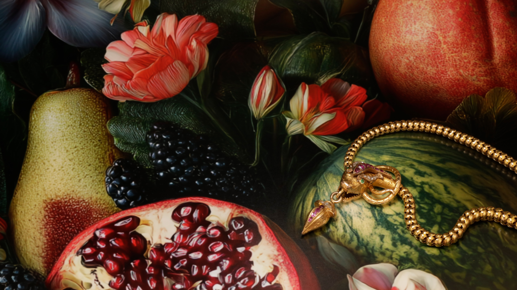Close-up of a colorful still-life with pomegranate, fruit, red flowers, and a gold beaded bracelet draped across the scene.