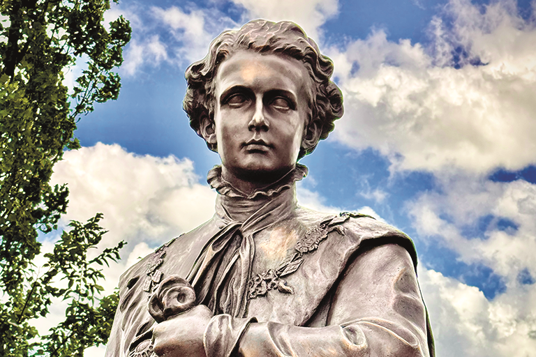 Darkened statue of a classical figure facing forward against a moody sky.