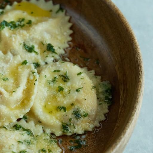 671033834_17875118394590987_6511983521437530148_n - IN München - Das Stadtmagazin Ravioli pasta tossed in garlic–herb butter with chopped parsley in a wooden bowl.