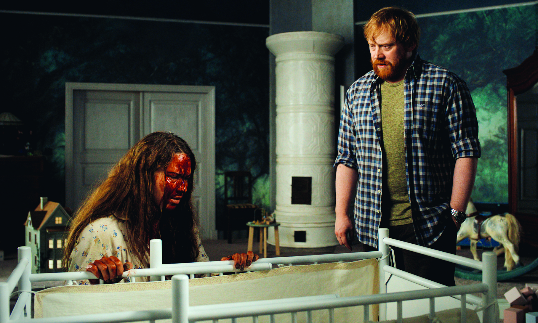 Bearded man in a blue plaid shirt stands over a seated woman with a bloody face in a dim, toy-filled room.